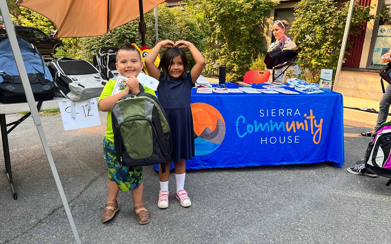Two children in front of a Sierra Community House table with backpacks